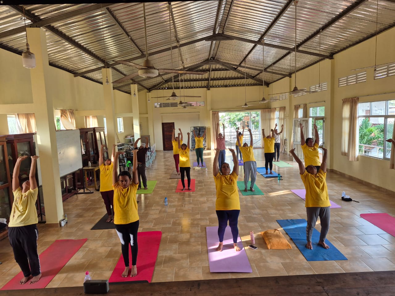 Academy students raising arms in a high-ceilinged shala